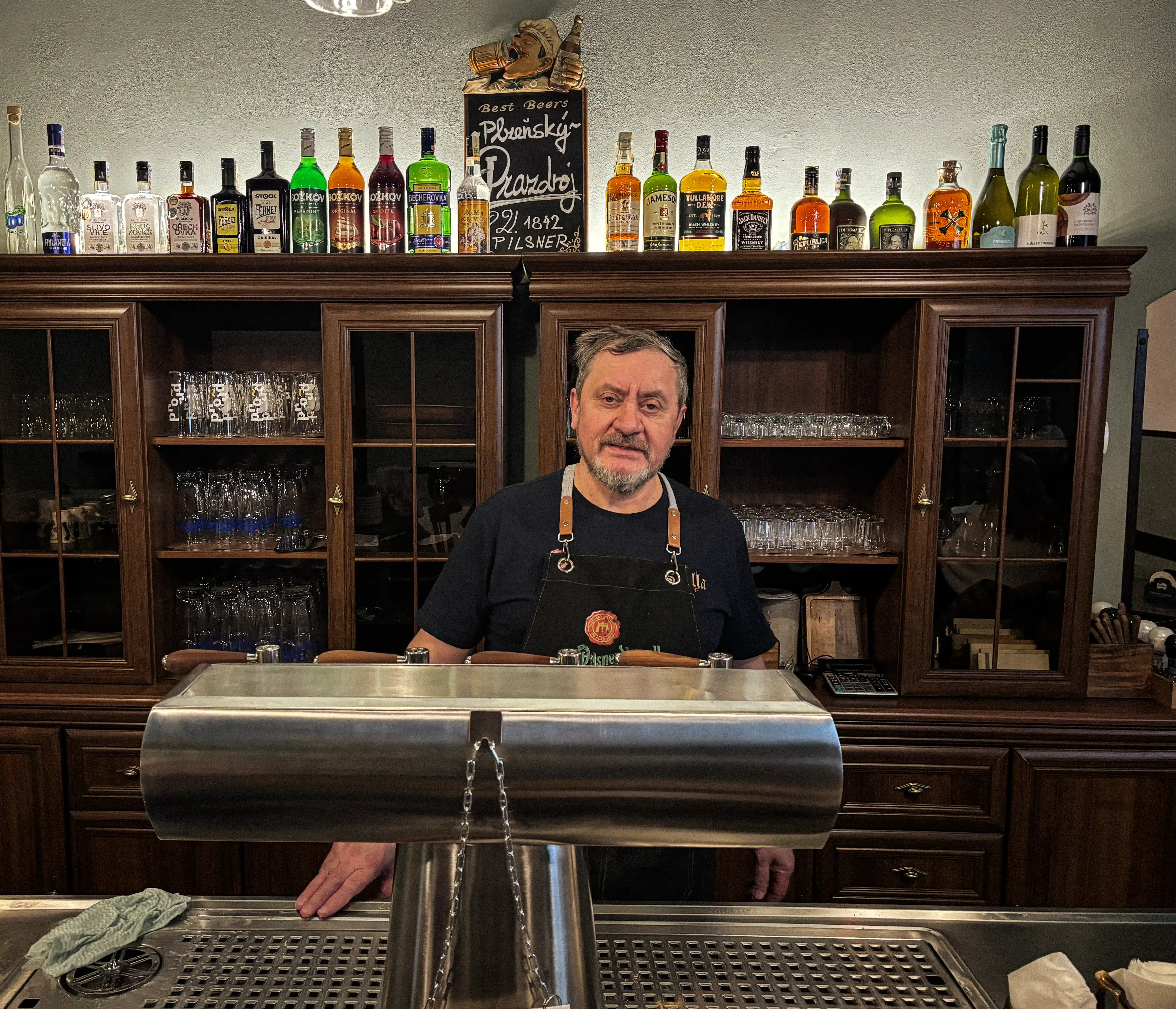 Šenkýř za barem hostince Školla s výčepem Plzeňského Prazdroje